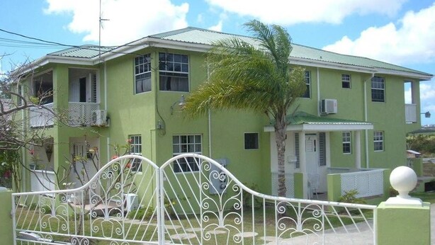 A two-story house with a green exterior, a white gate, and a palm tree in the yard. - Malfranza Apartments (Bridgetown)