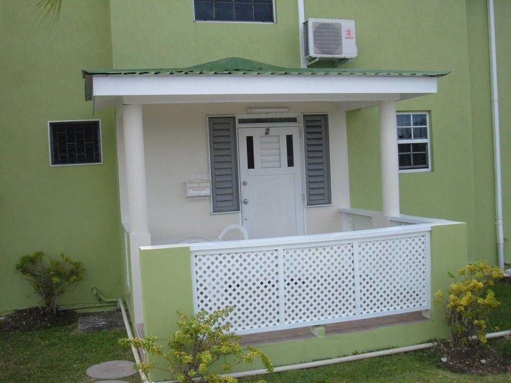 A small building with a green exterior, a white door, and a white balcony with a lattice railing.