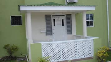 A small building with a green exterior, a white door, and a white balcony with a lattice railing.