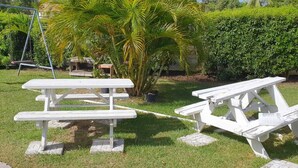 Two white picnic tables in a grassy area with a swing set and a palm tree in the background. - Malfranza Apartments (Bridgetown)
