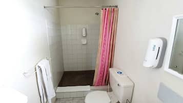 Un baño pequeño con ducha, inodoro y dispensador de jabón.