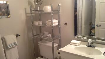 Un baño con inodoro, lavamanos y un estante metálico con toallas y artículos de aseo.