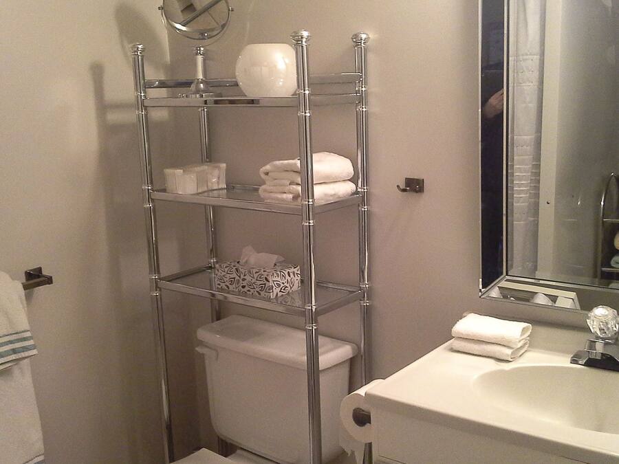 Un baño con inodoro, lavamanos y un estante metálico con toallas y artículos de aseo.