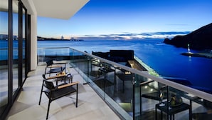 A modern balcony with glass railings overlooking a body of water and distant cityscape.