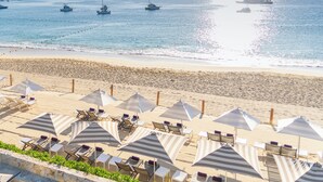 A beach with rows of sun loungers and umbrellas, a clear sky, and several boats on the water.