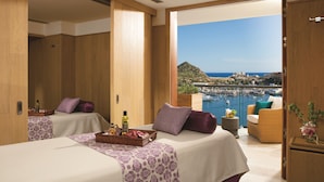 A hotel room with two beds, a balcony with a view of the sea and boats, and a wooden interior.