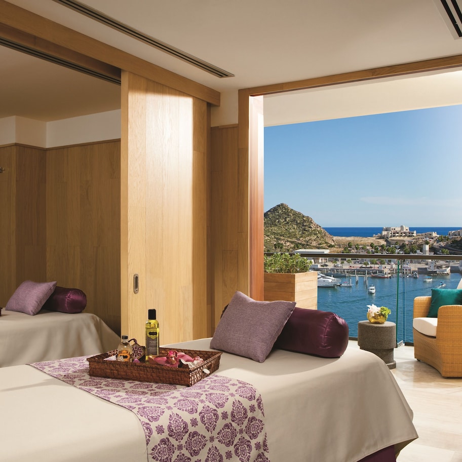 A hotel room with two beds, a balcony with a view of the sea and boats, and a wooden interior.