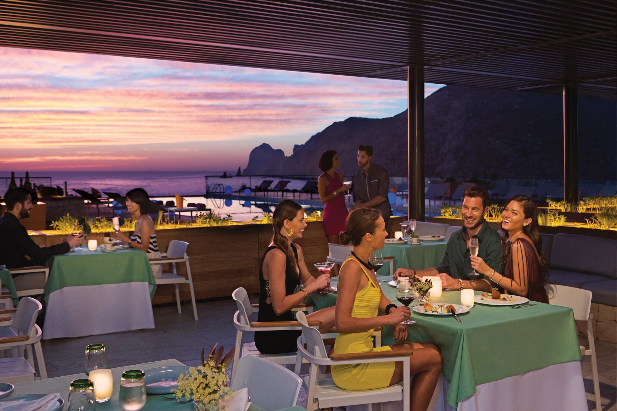 An outdoor dining area with tables set for a meal, overlooking a scenic view of the ocean and mountains.