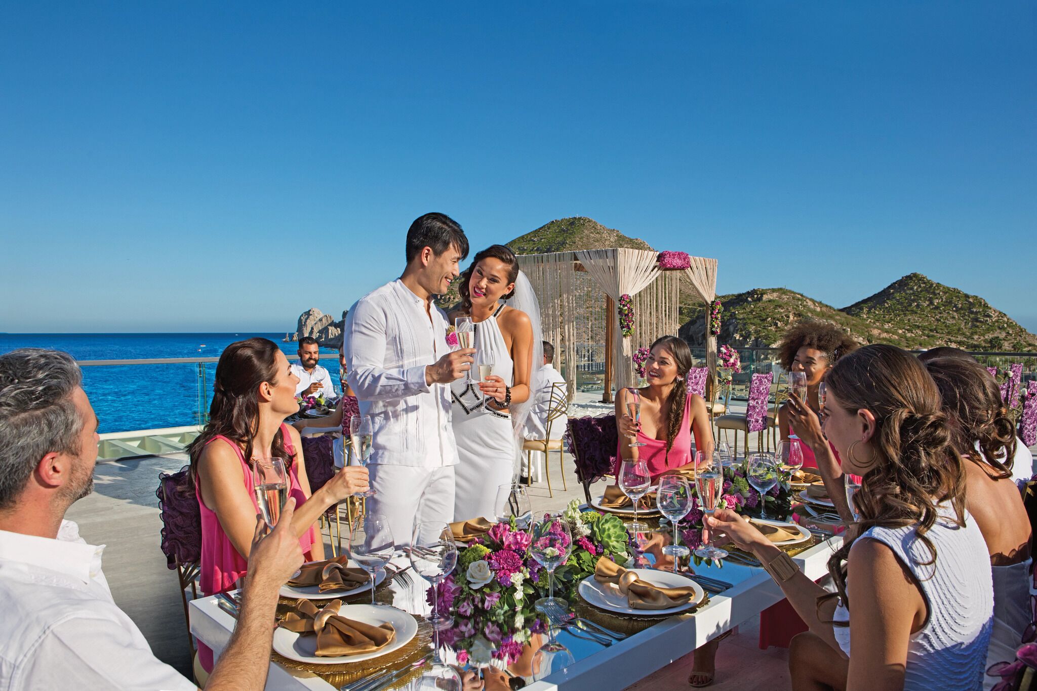 A group of people dining on a boat with a view of the sea and hills in the background.