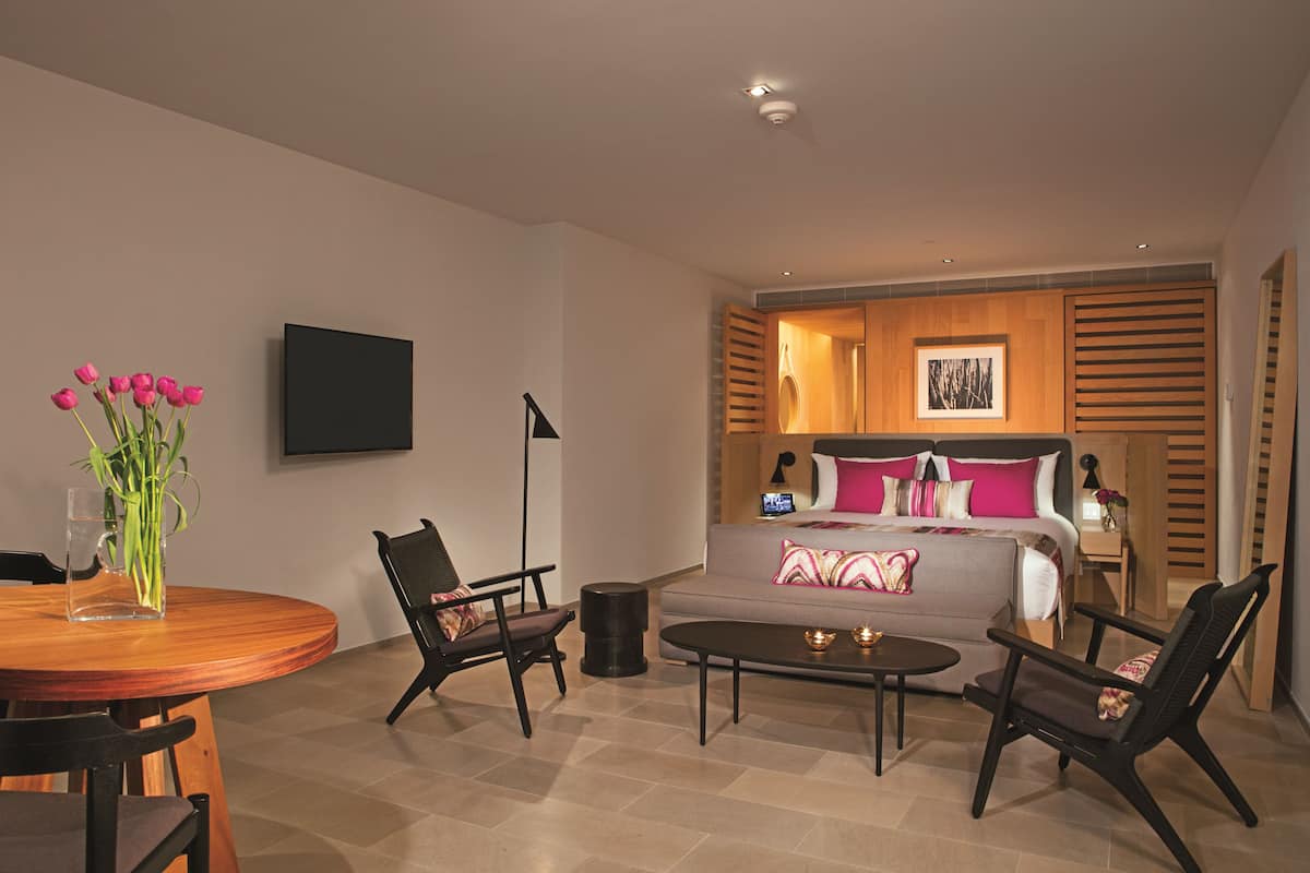 Una habitación de hotel moderna con cama, sofá, mesa de comedor y dos sillas.