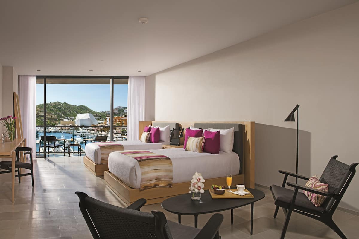 Una habitación de hotel moderna con una cama grande, un escritorio, una silla y vistas a un puerto deportivo.