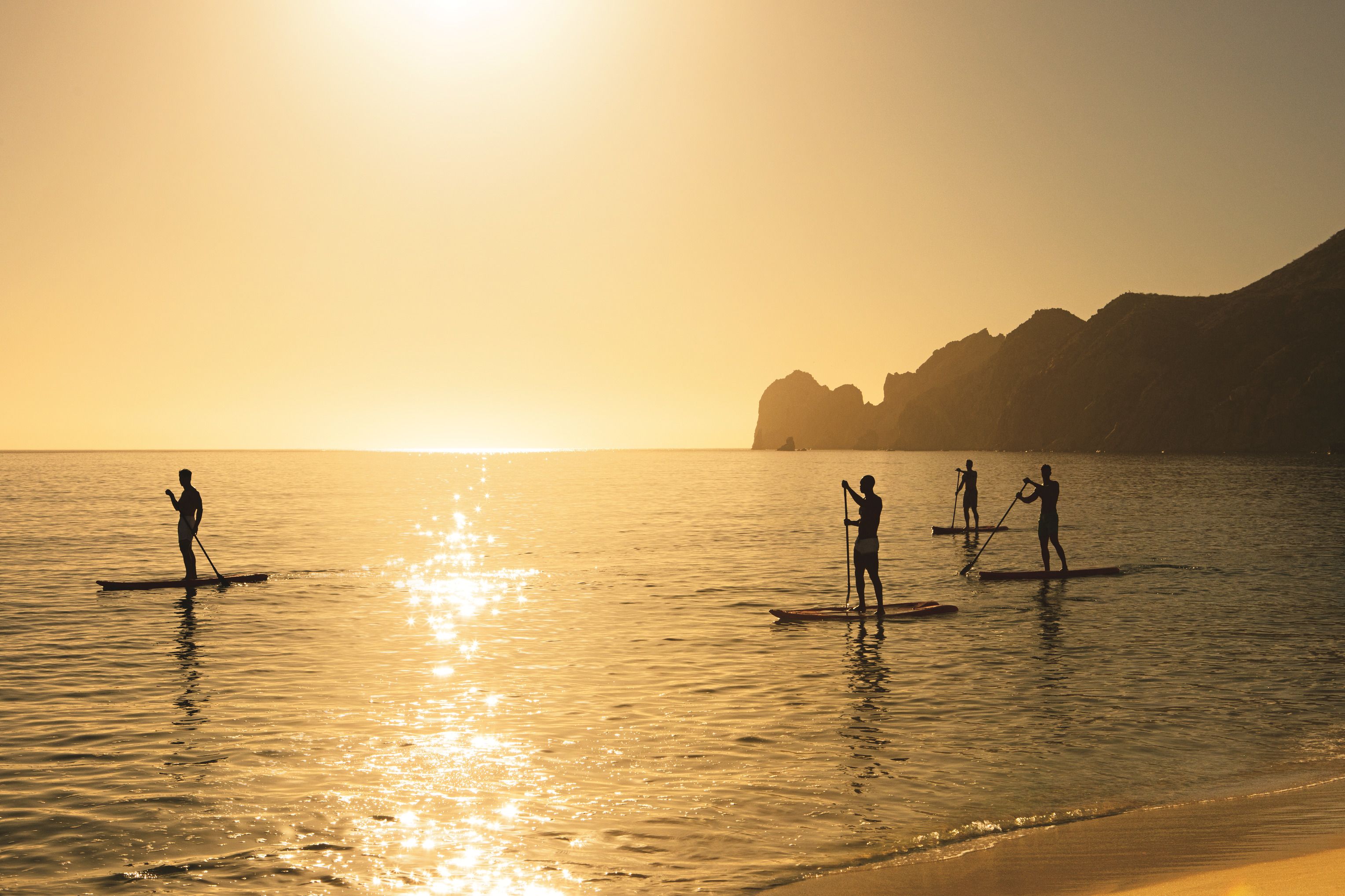 A sunset over a calm sea with people paddleboarding.