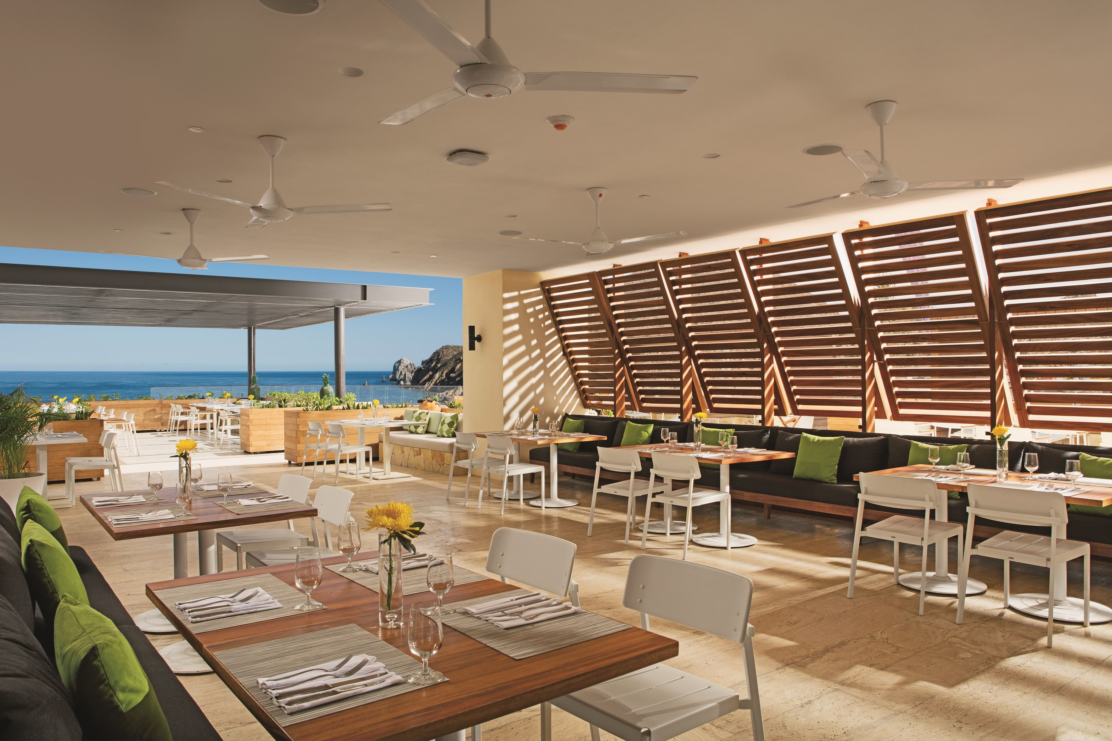 Un restaurante con terraza, mobiliario blanco y vistas al océano.