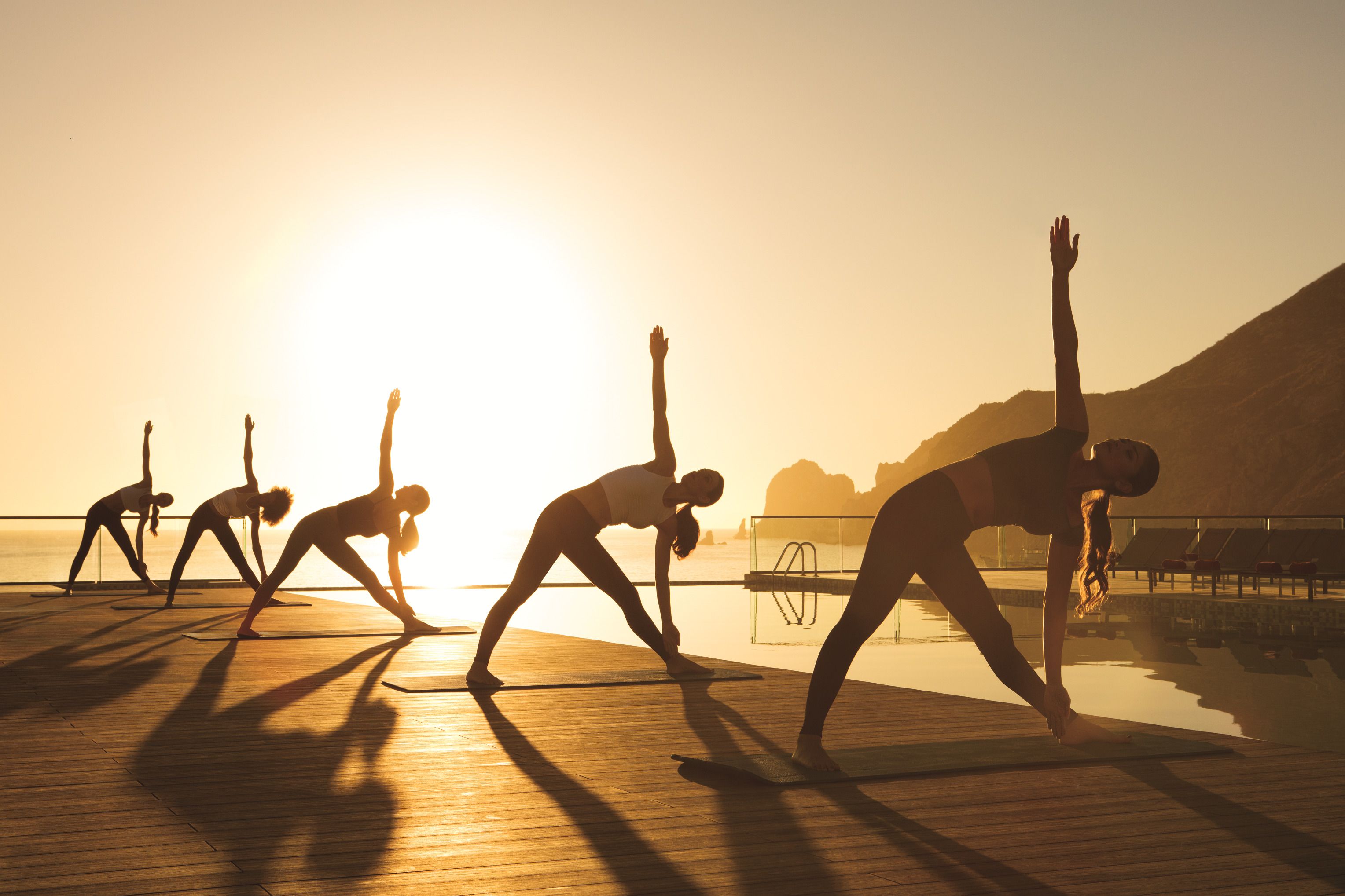 Een groep mensen doet yoga op een houten terras aan het water tijdens de zonsondergang.