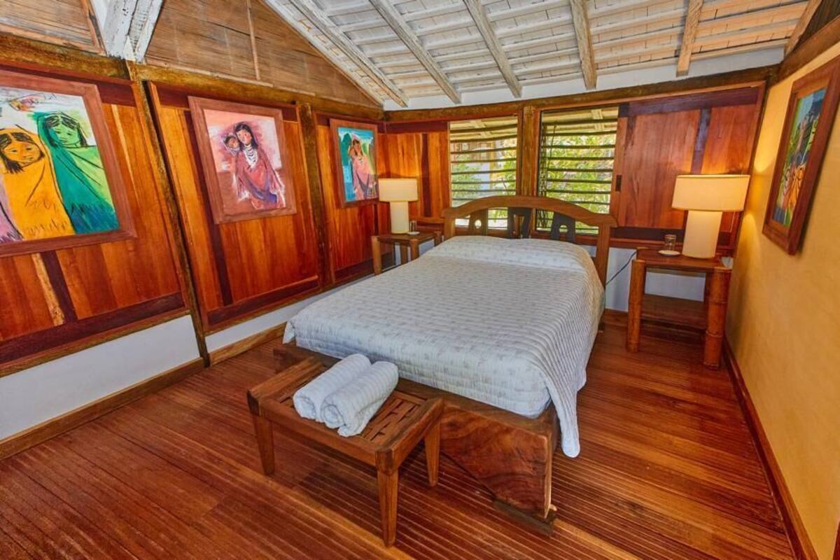 A wooden-floored bedroom with a bed, bedside tables, and artwork on the walls.