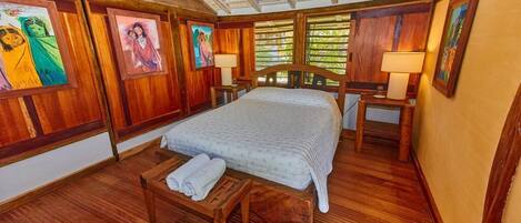 A wooden-floored bedroom with a bed, bedside tables, and artwork on the walls.