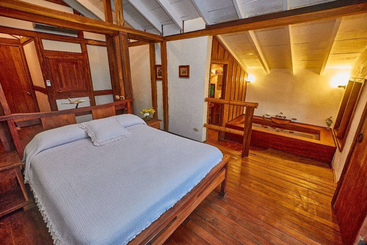 A bedroom with a wooden bed, a wooden staircase, and a view of a bathroom.