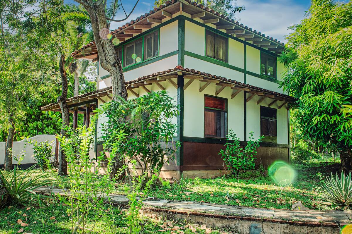 A two-story house with a tiled roof, surrounded by lush greenery.