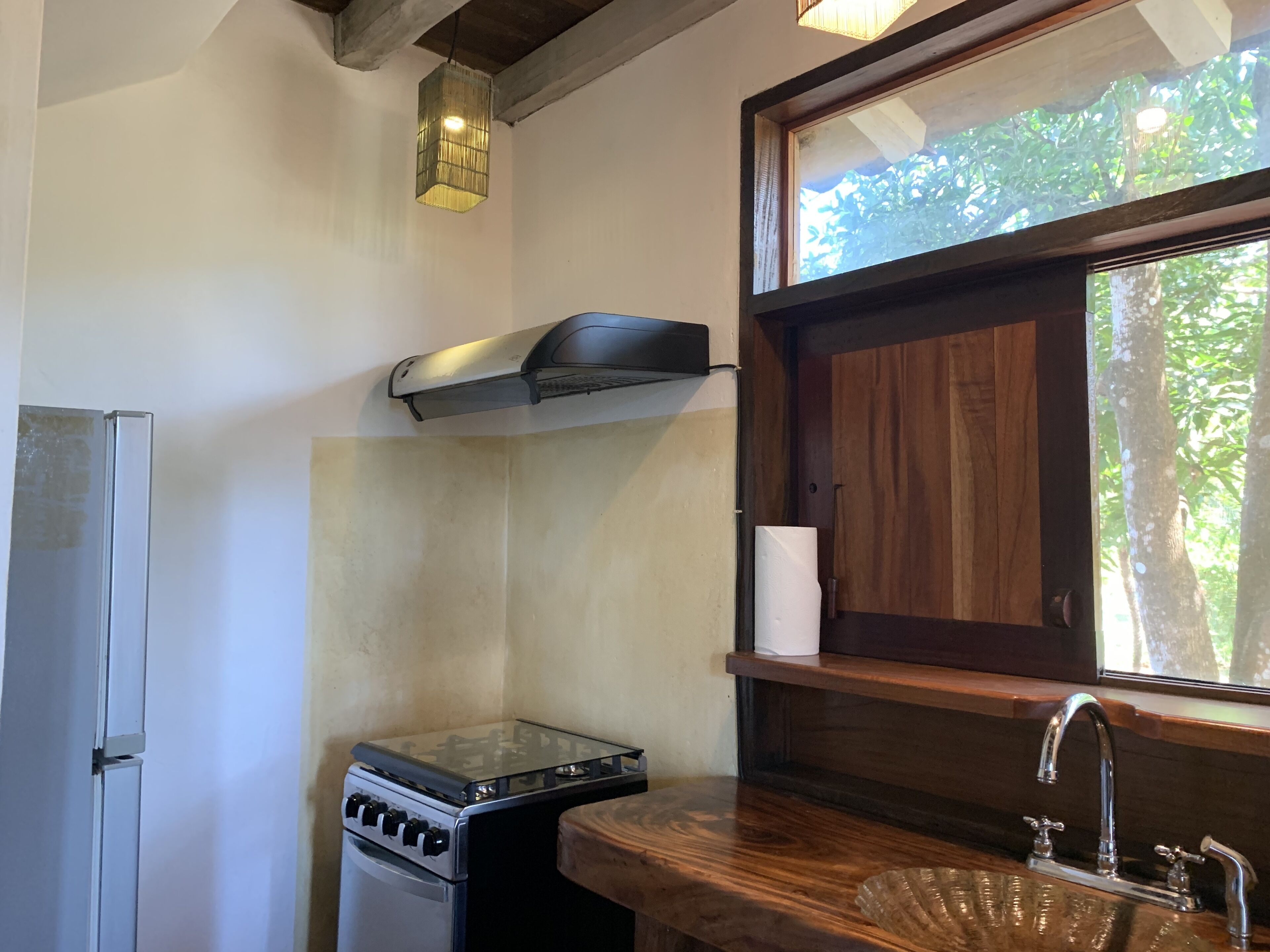 A compact kitchen with a gas stove, a refrigerator, a wooden countertop, a sink, and a window with a view of greenery.