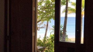 Un dormitorio con cama, una puerta de madera y vistas a la playa y al océano a través de una ventana.