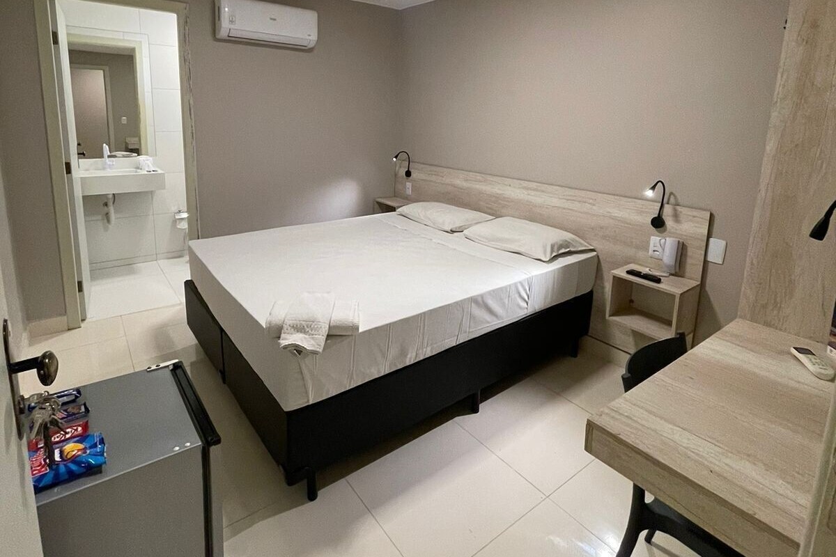 Een slaapkamer met een bed, nachtkastje, bureau en een kleine koelkast.