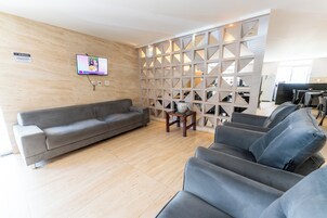Sala de estar moderna com um sofá cinza, TV fixada na parede e um divisória decorativo com padrões geométricos.