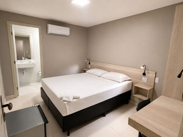 Un dormitorio con cama, mesitas de noche, un escritorio y un equipo de aire acondicionado.