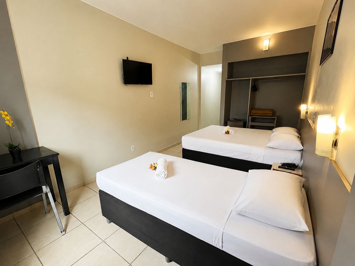 A hotel room with two beds, a desk, a TV, and a mirror.
