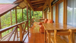A wooden deck with a table and chairs, overlooking lush greenery. - Hotel Holístico Monteverde (Monteverde)