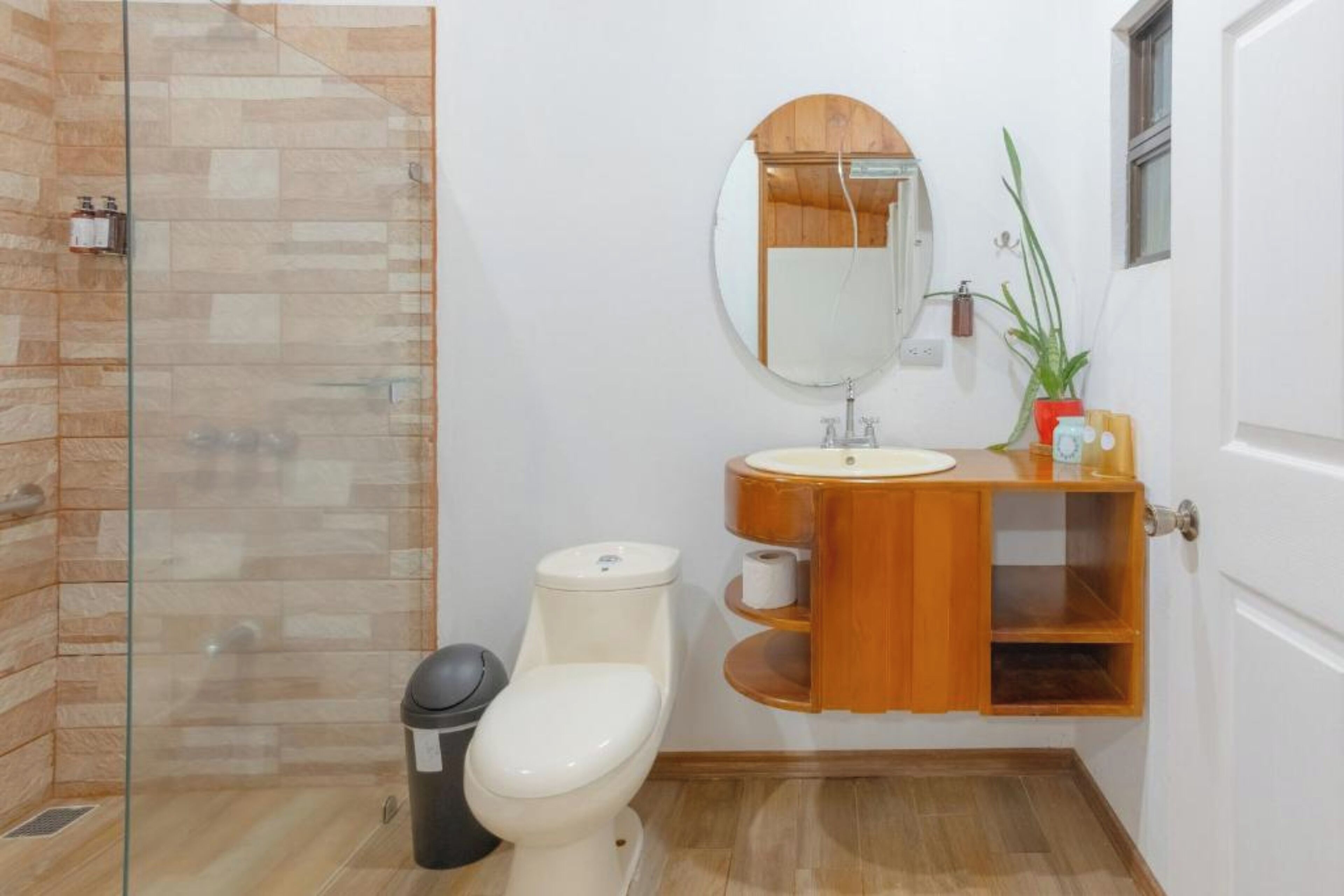 A bathroom with a glass shower enclosure, a toilet, a sink with a wooden vanity, and a mirror.
