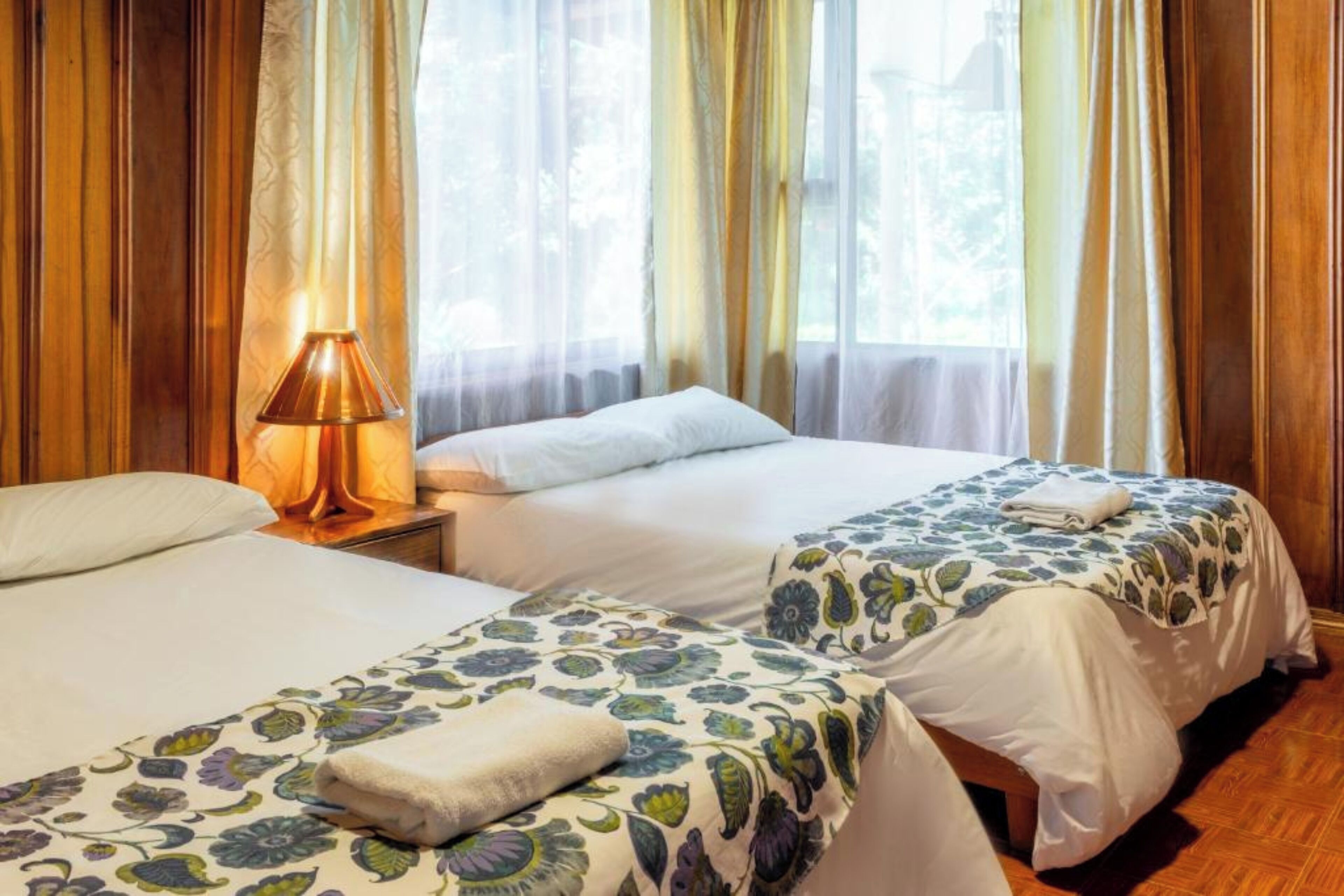 Una habitación de hotel con dos camas, una lámpara y un ventanal con cortinas.