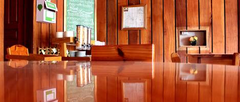 Un interior de madera con una mesa pulida, un panel de menú verde y un mapa enmarcado.
