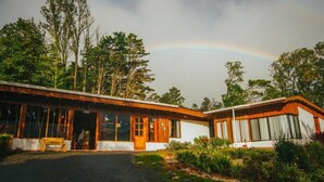 A modern building with large windows and a wooden exterior, surrounded by lush greenery and a visible rainbow in the sky. - Hotel Holístico Monteverde (Monteverde)