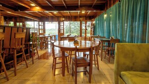 A wooden interior with a round table and chairs, a sofa, and large windows offering a view of greenery. - Hotel Holístico Monteverde (Monteverde)