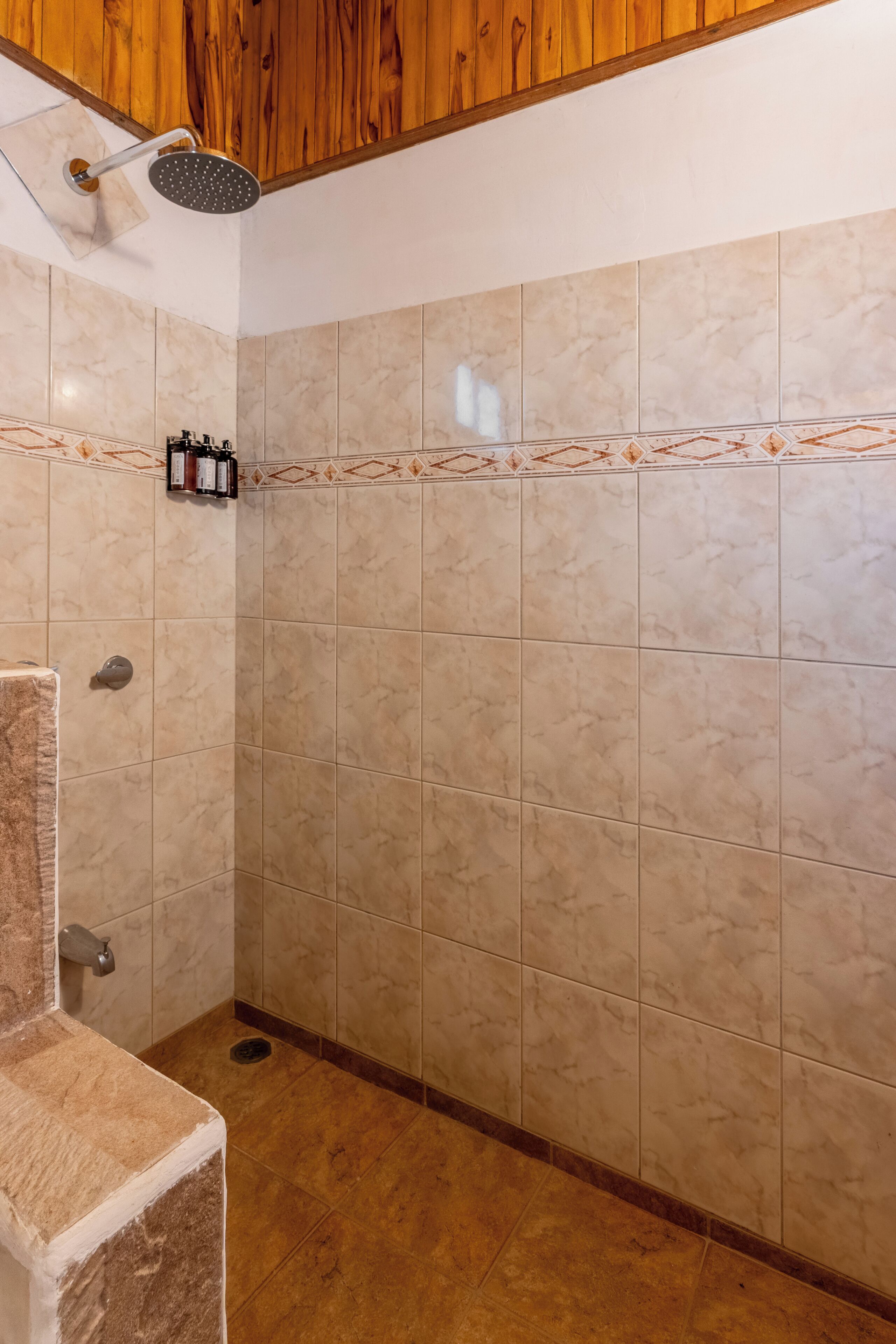 A bathroom with a shower, tiled walls, and a wooden ceiling.