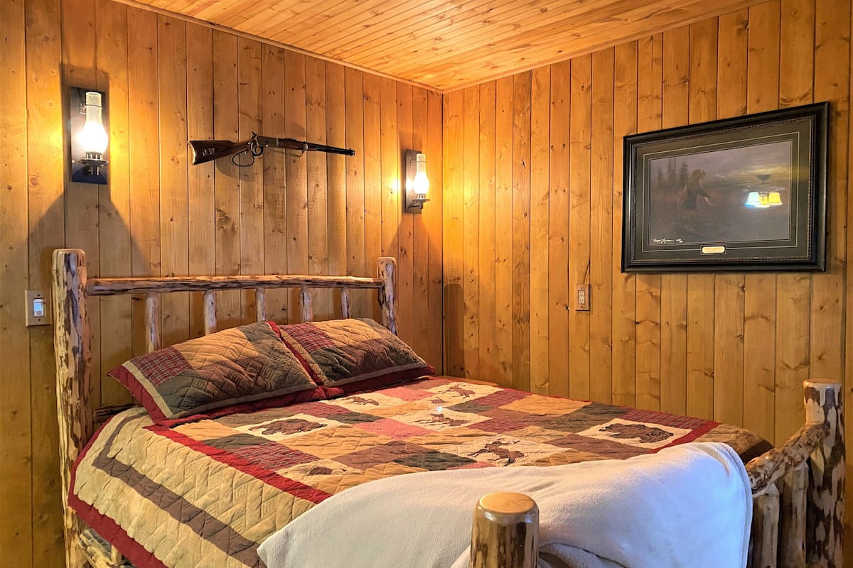 A wooden-paneled room with a bed, two wall-mounted lights, and a framed picture on the wall.