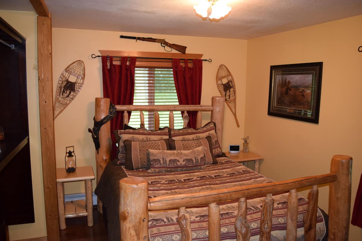 A wooden bed with patterned bedding, a small bedside table, a wall-mounted fan, and a framed picture on the wall.