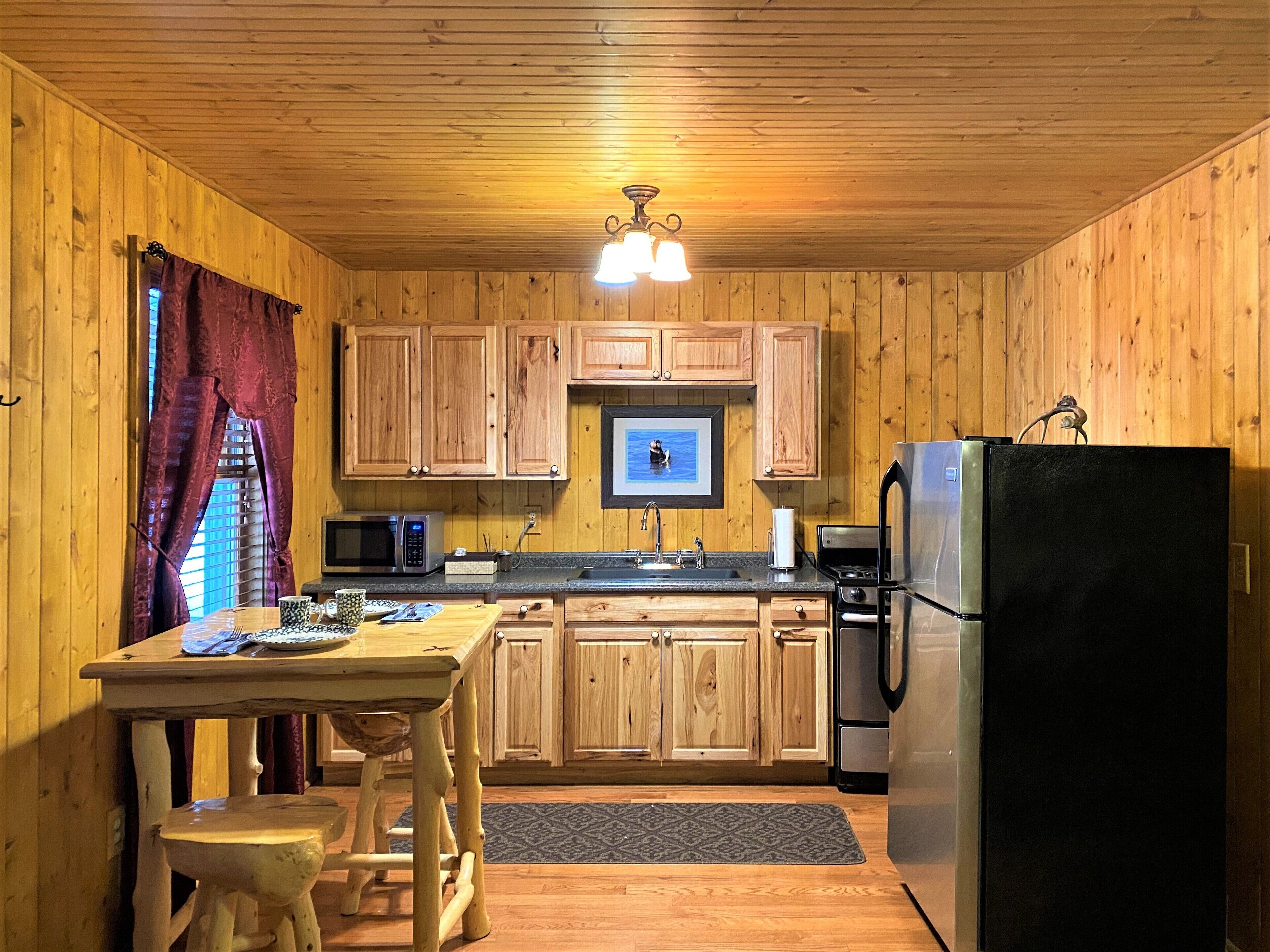A wooden-paneled kitchen with a wooden table, a microwave, a refrigerator, and a sink.