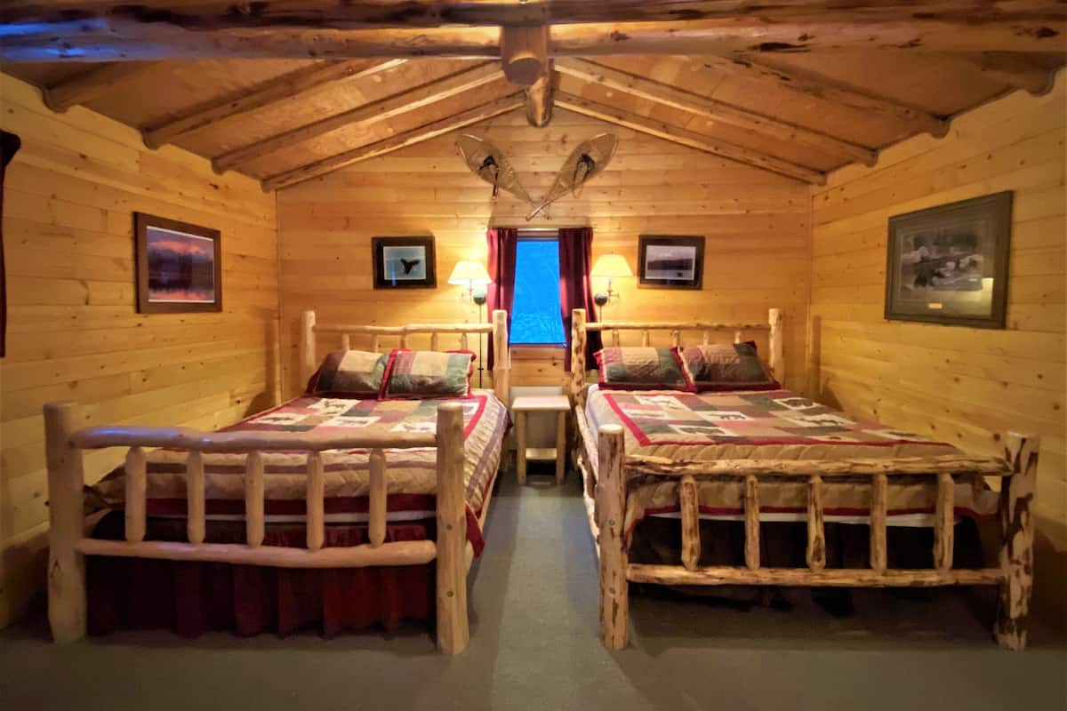 A cabin with two wooden beds, a ceiling fan, and framed pictures on the walls.