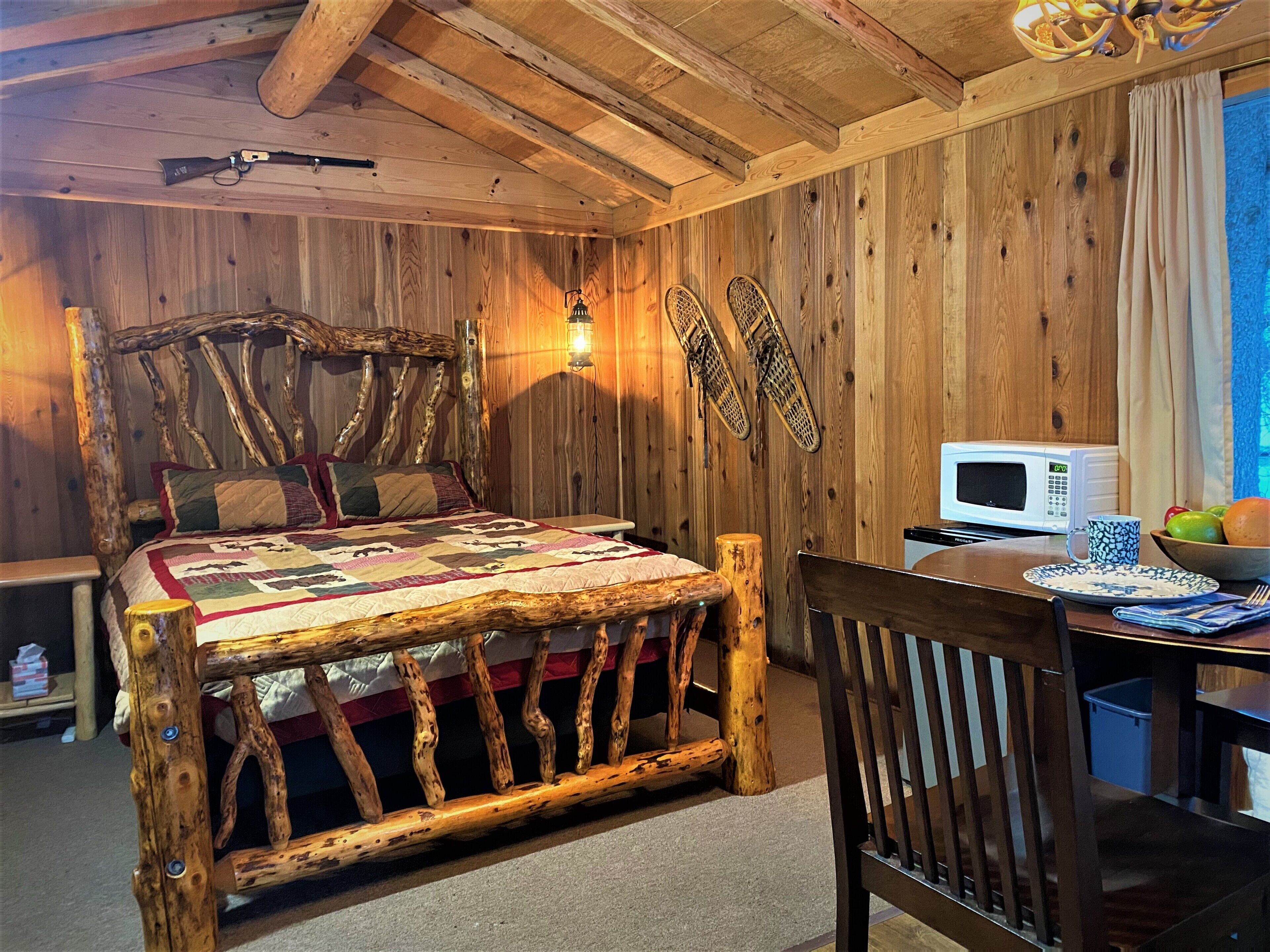 A rustic room with a wooden bed, a wooden desk, a microwave, and a bowl of fruit.