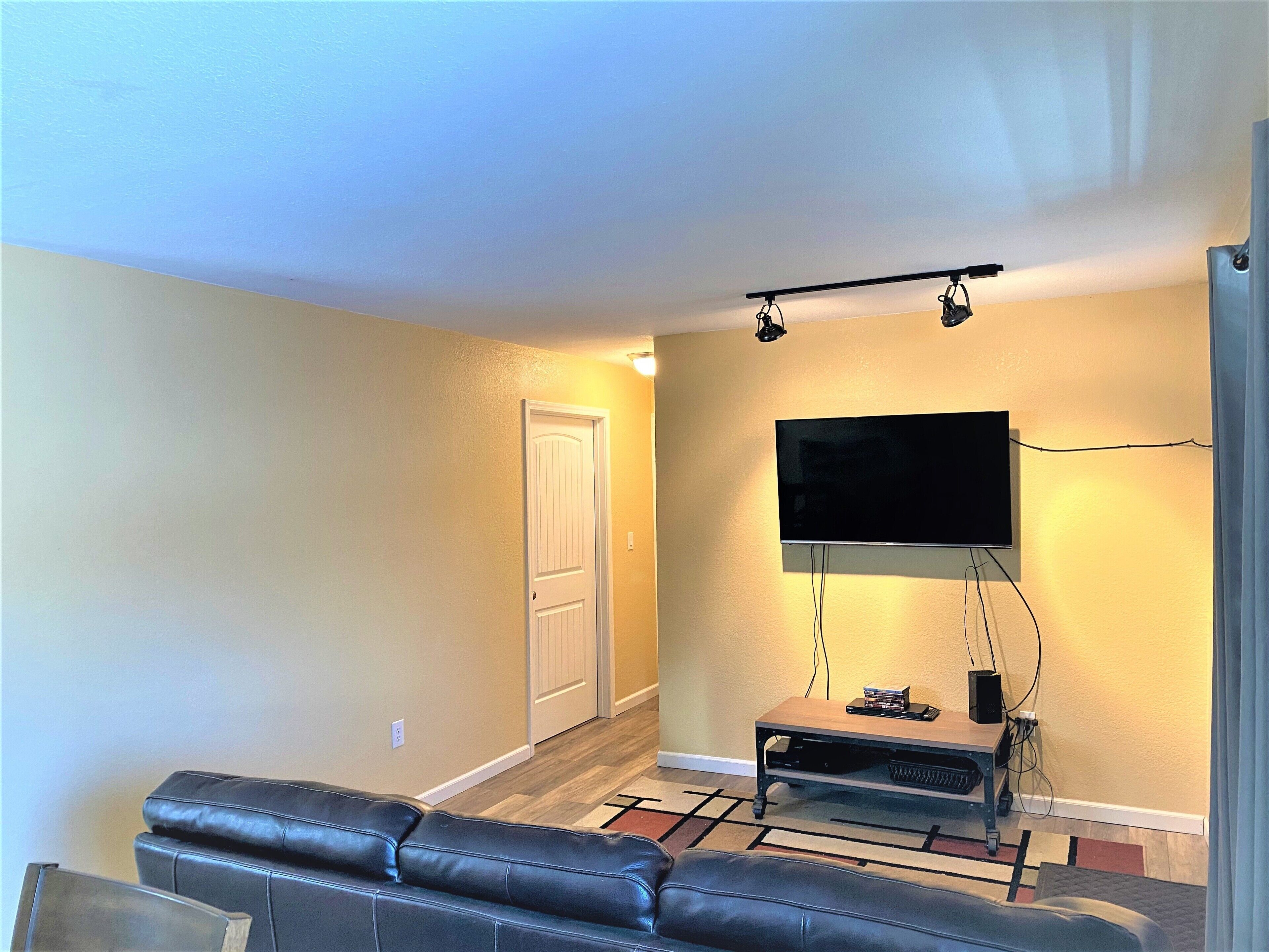 A living room with a black leather couch, a flat-screen TV mounted on the wall, and a wooden coffee table.