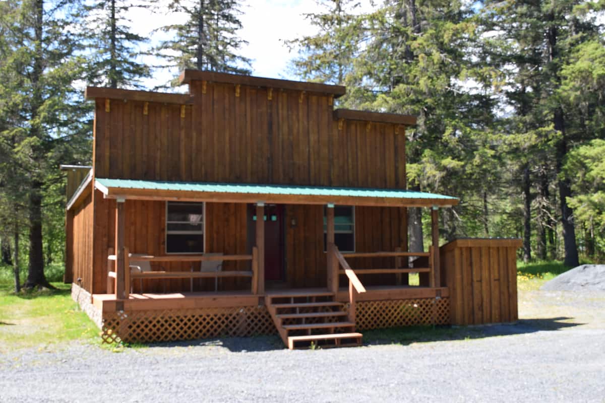A wooden cabin with a porch, a front door, and a small set of stairs leading up to the entrance.