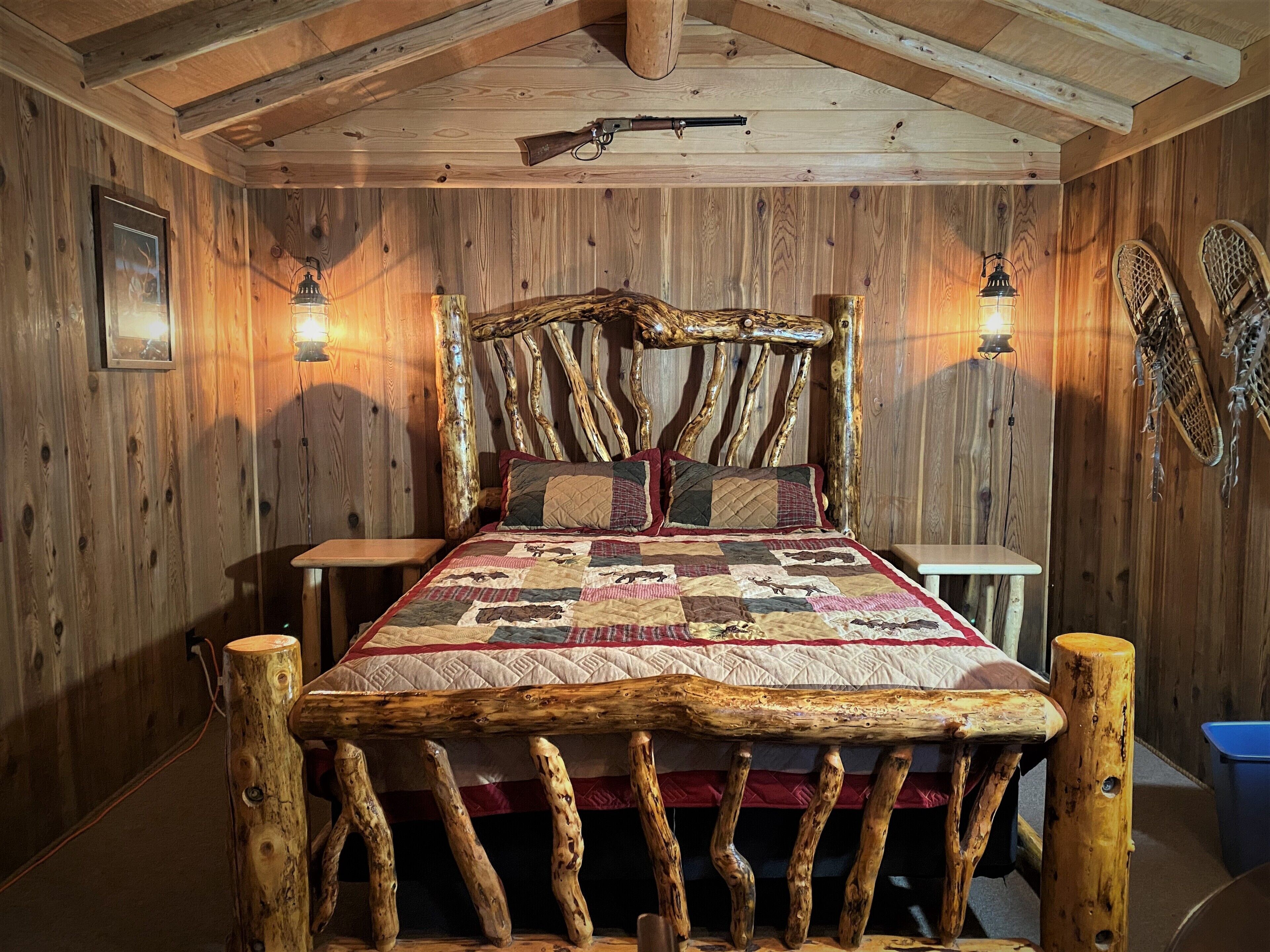 A rustic wooden room with a bed featuring a unique log headboard and a quilted bedspread.