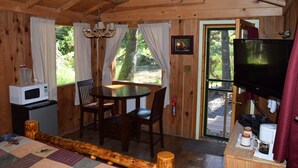 Interior acogedor de una cabaña con una mesa de madera, sillas, televisor, microondas y cafetera.