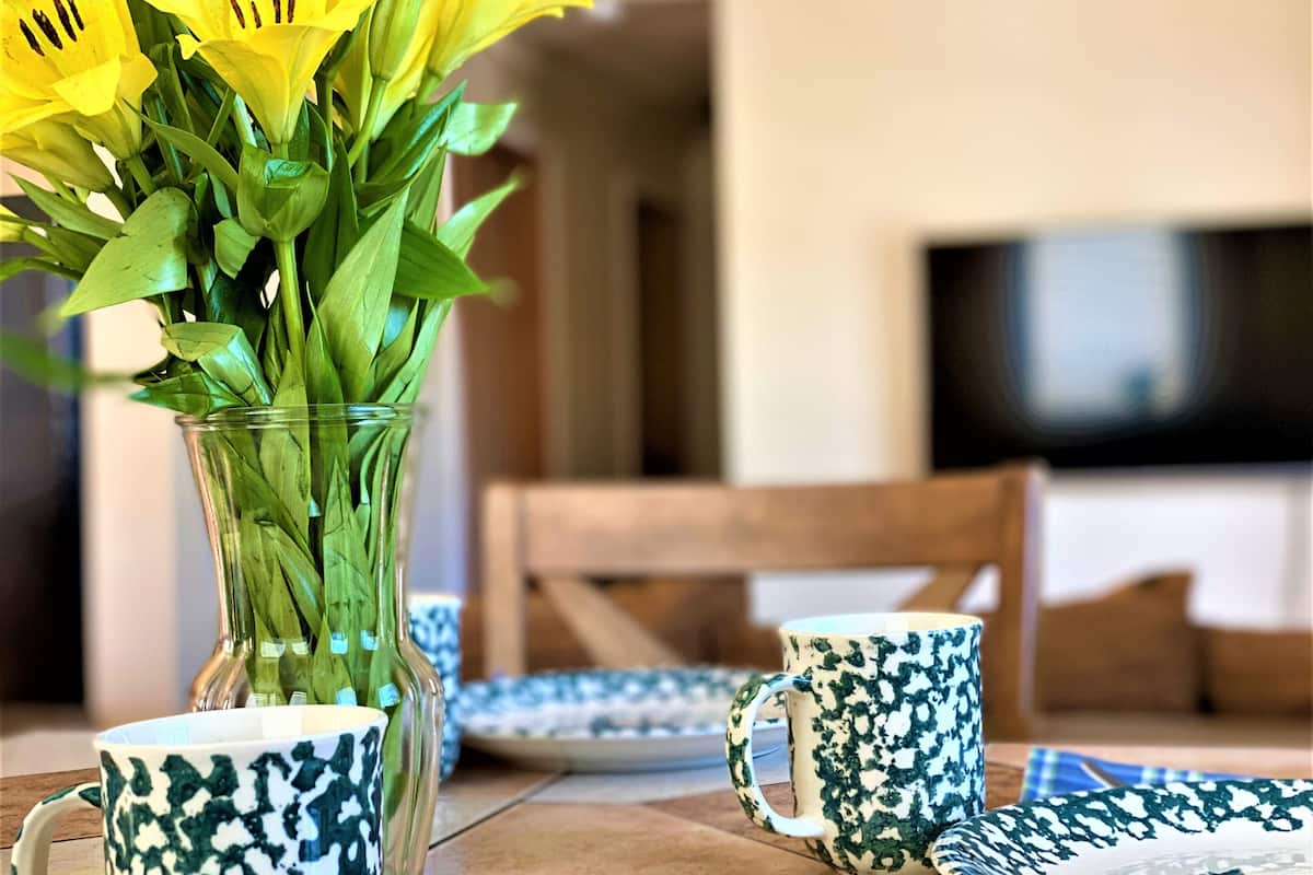 A dining table with a vase of yellow flowers, a patterned mug, and a plate with a floral design.
