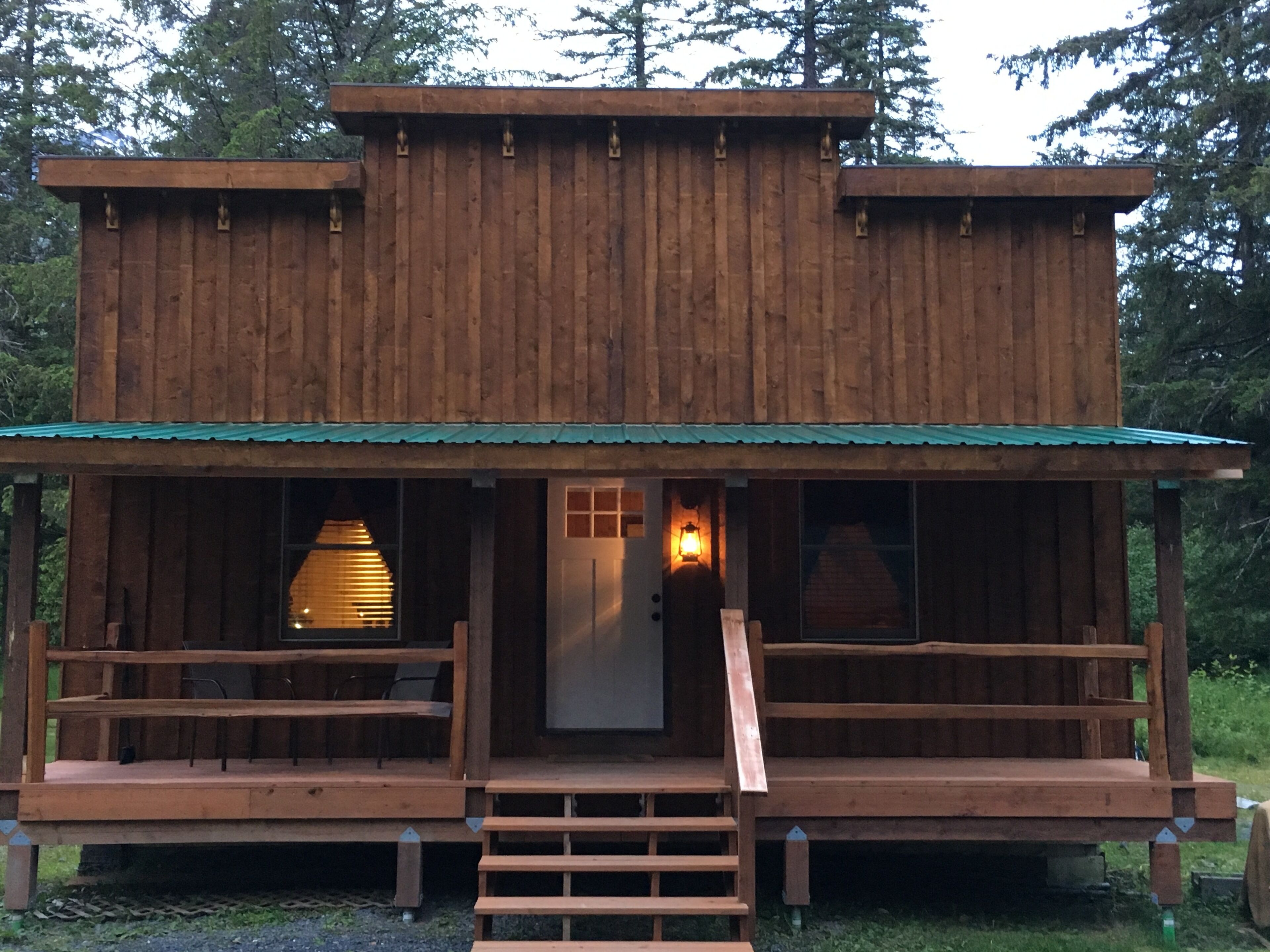 A wooden cabin with a porch, a staircase leading to the entrance, and a window with blinds.