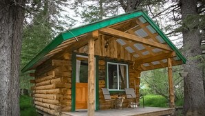 Una cabaña de troncos con un porche, una ventana y una puerta.