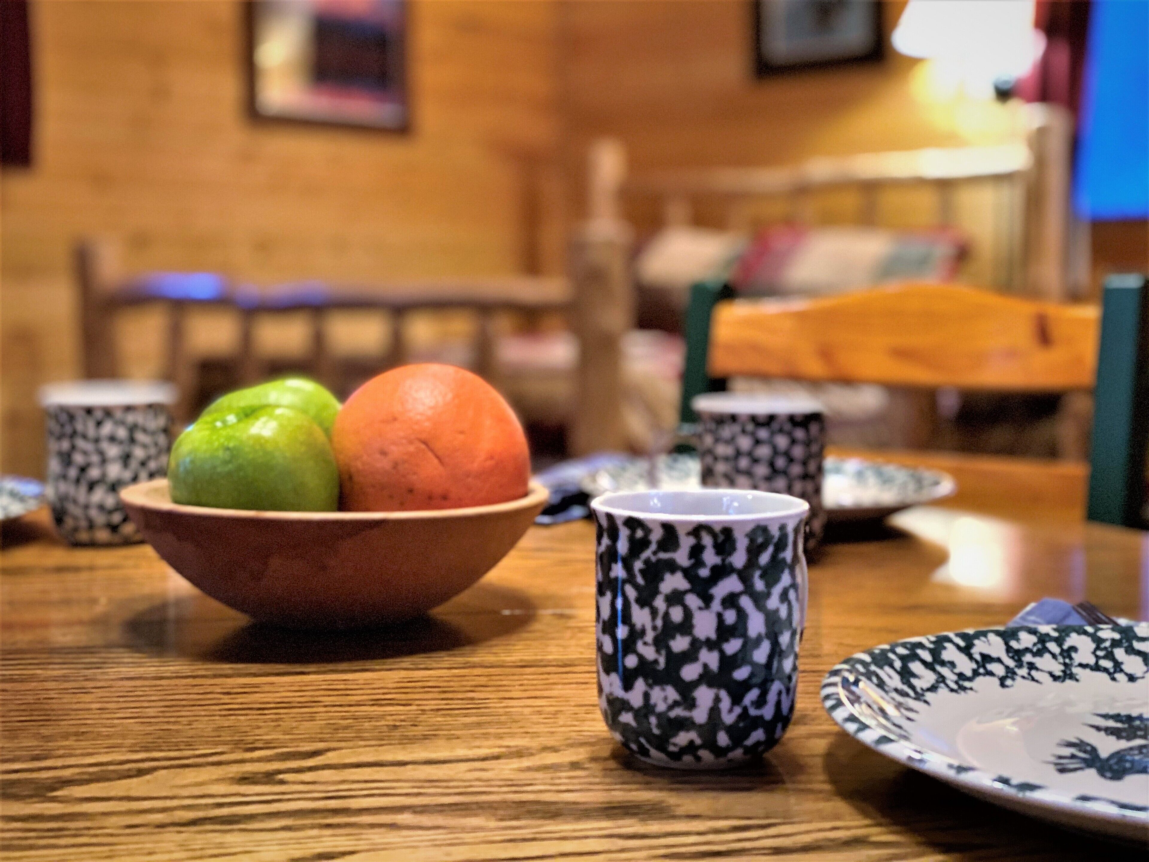 A dining table with a bowl containing two fruits, a patterned cup, and a plate.