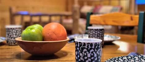 Uma mesa de jantar com uma tigela contendo duas frutas, uma xícara estampada e um prato.