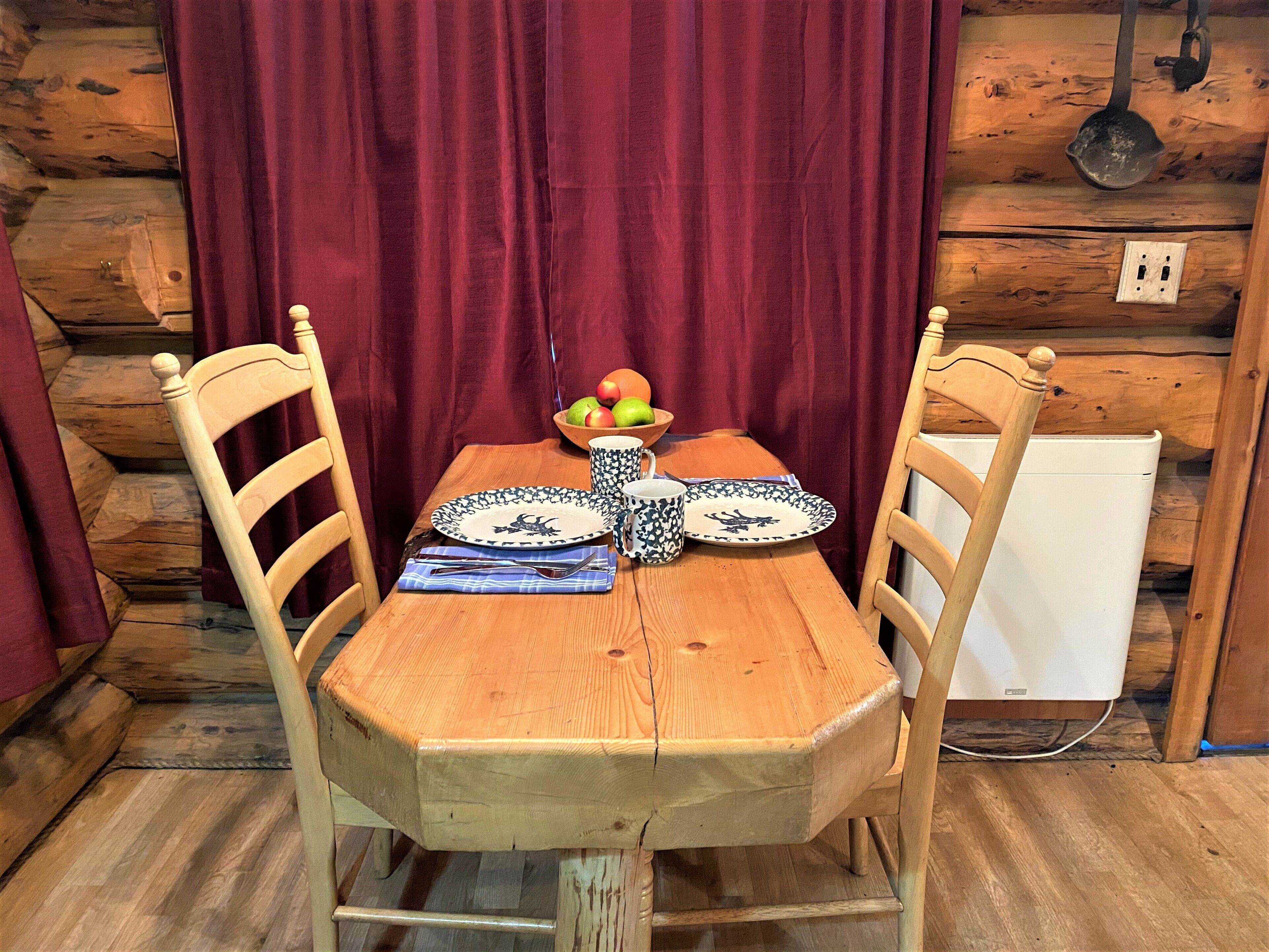A wooden dining table with two chairs, a bowl of fruit, and plates with a blue pattern.